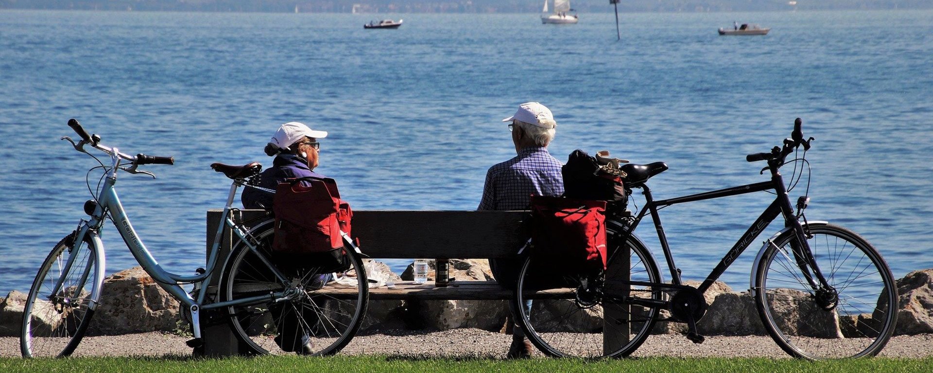Nahaufnahme von zwei Fahrradfahrern, die auf einer Bank am Bodensee Pause machen.