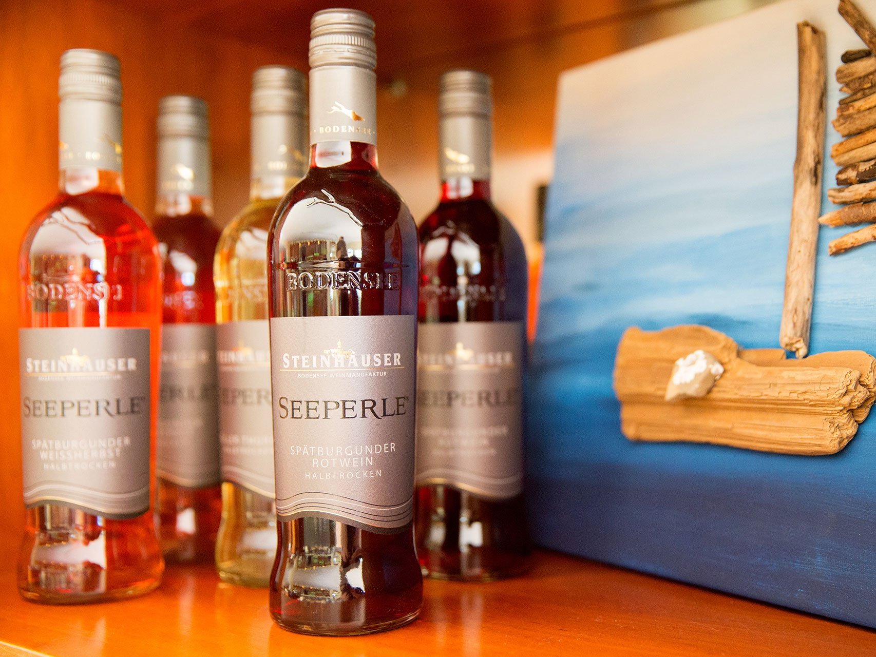 Mehrere Flaschen Rotwein aus dem Hottel Seeperle stehen nebeneinander im Regal.